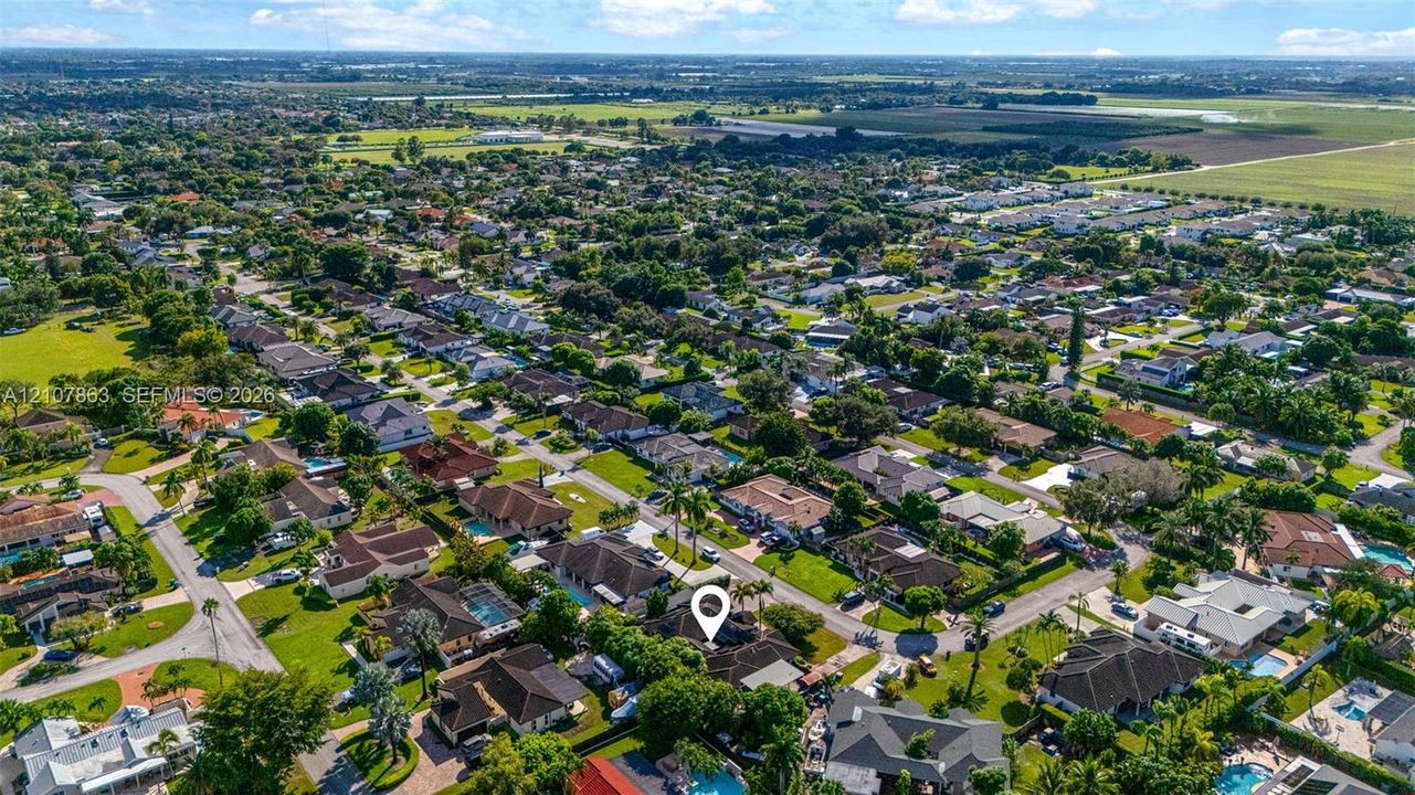 Aerial perspective of a residential neighborhood featuring mature landscaping, grid-patterned streets, and expansive surrounding agricultural acreage