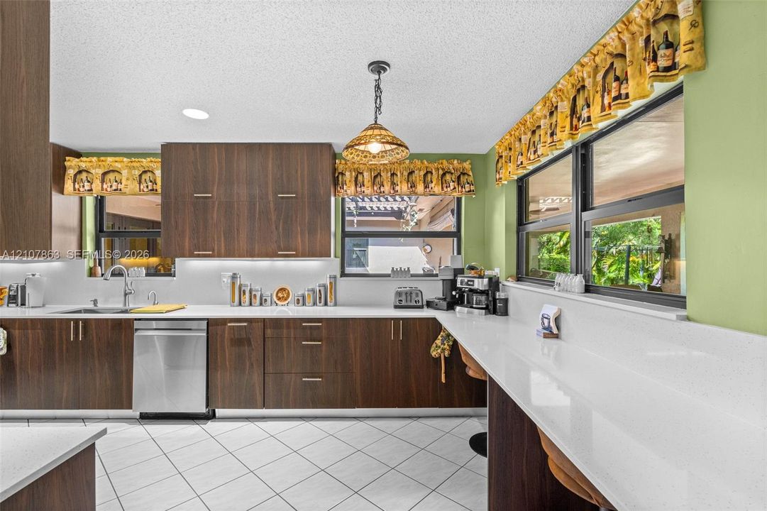 Kitchen featuring wood-finish cabinetry, white solid-surface countertops, stainless steel dishwasher, pendant lighting, and ceramic tile flooring