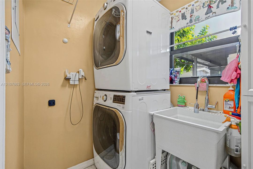 Laundry area featuring a stackable washer and dryer, a deep utility sink with a pull-down faucet, and a large window