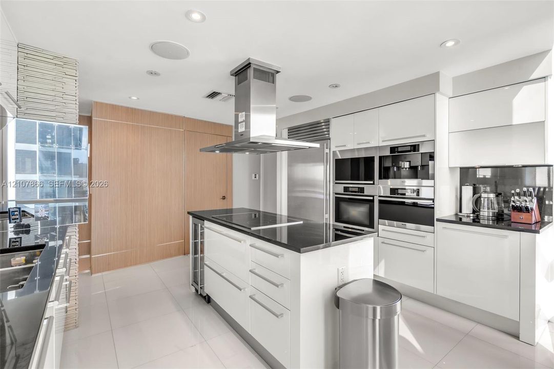 Contemporary kitchen featuring high-gloss white cabinetry, polished stone countertops, stainless steel professional-grade appliances, a central island with a glass-ceramic cooktop, and recessed ceiling lighting