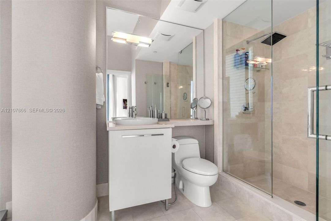 Bathroom featuring a white vanity with a vessel sink, a full-length wall mirror, a glass-enclosed walk-in shower with stone-tile surround, and a rain-style showerhead