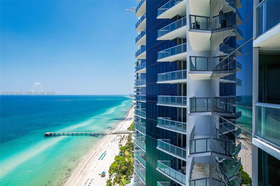 High-rise exterior featuring glass curtain walls and private cantilevered balconies with glass railings overlooking the coastline