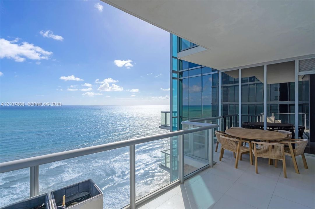 Covered balcony featuring white tile flooring, glass panel railings, and floor-to-ceiling glass wall panels overlooking the ocean