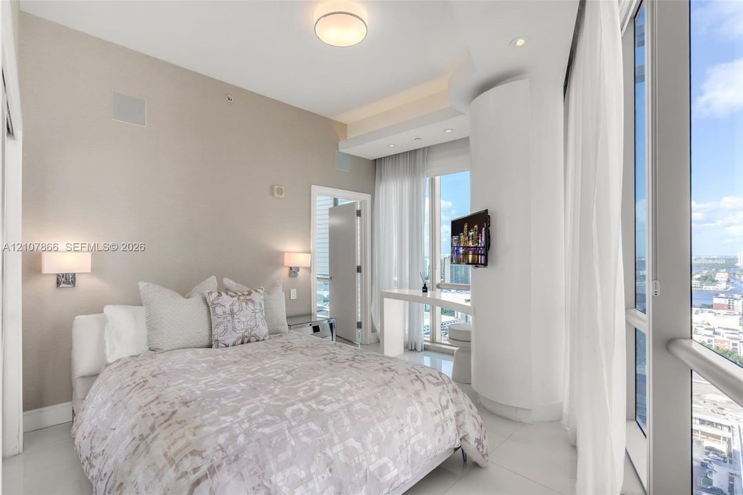 Floor-to-ceiling windows, neutral interior wall palette, polished tile flooring, recessed ceiling lighting, and built-in wall-mounted bedside fixtures