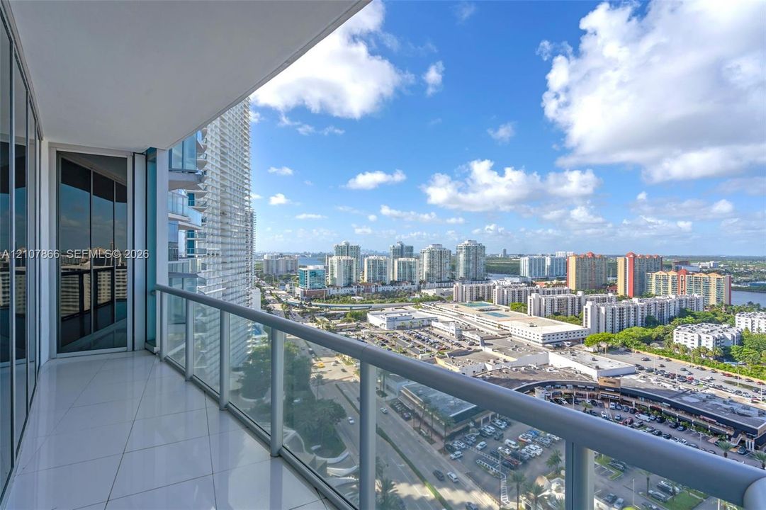 Covered balcony featuring white tile flooring, floor-to-ceiling glass paneling, and a metal railing