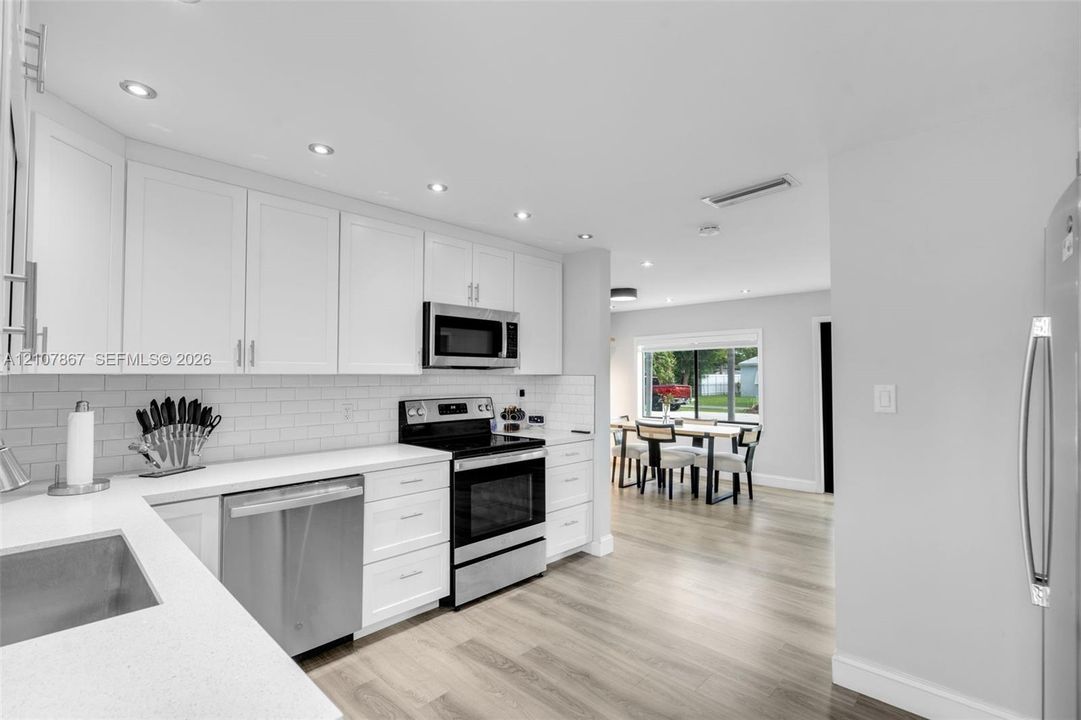 Kitchen featuring white Shaker-style cabinetry, white solid-surface countertops, a subway tile backsplash, stainless steel appliances, and recessed lighting
