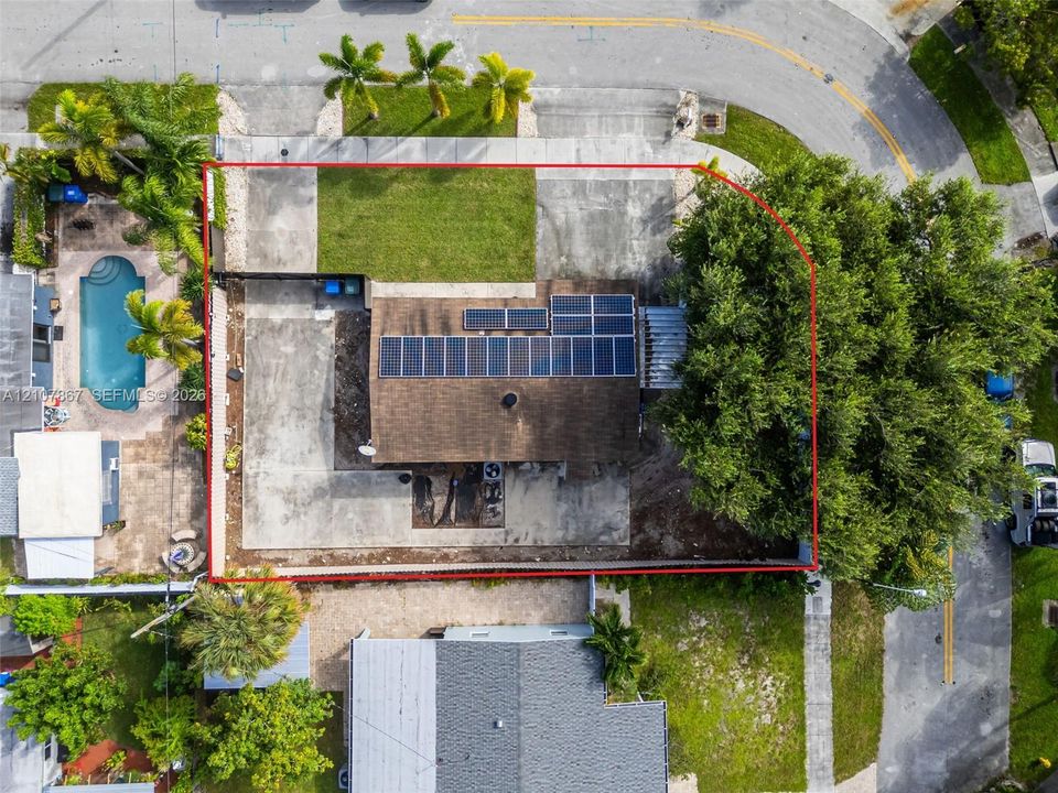 Aerial perspective of property featuring solar panel array, concrete driveway, fenced perimeter, and mature tree canopy