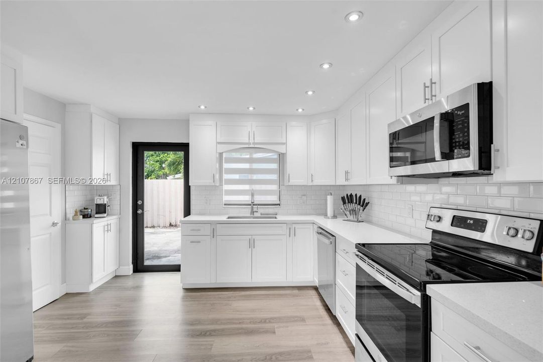 Kitchen featuring white shaker-style cabinetry, quartz countertops, white subway tile backsplash, stainless steel appliances, and wood-finish flooring