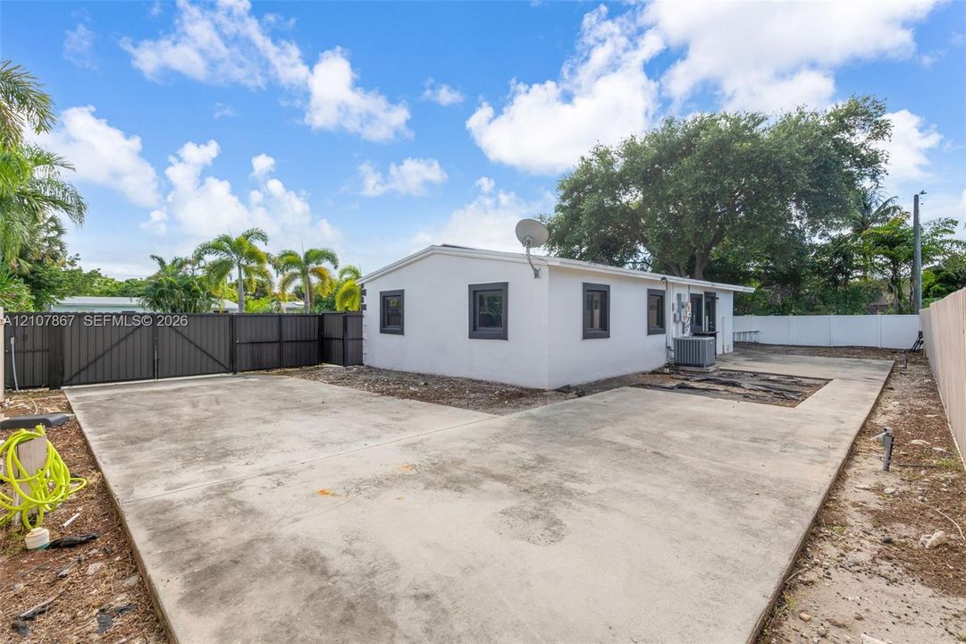 Exterior featuring a concrete patio, dark-toned metal privacy fencing, white siding, and dark-framed windows