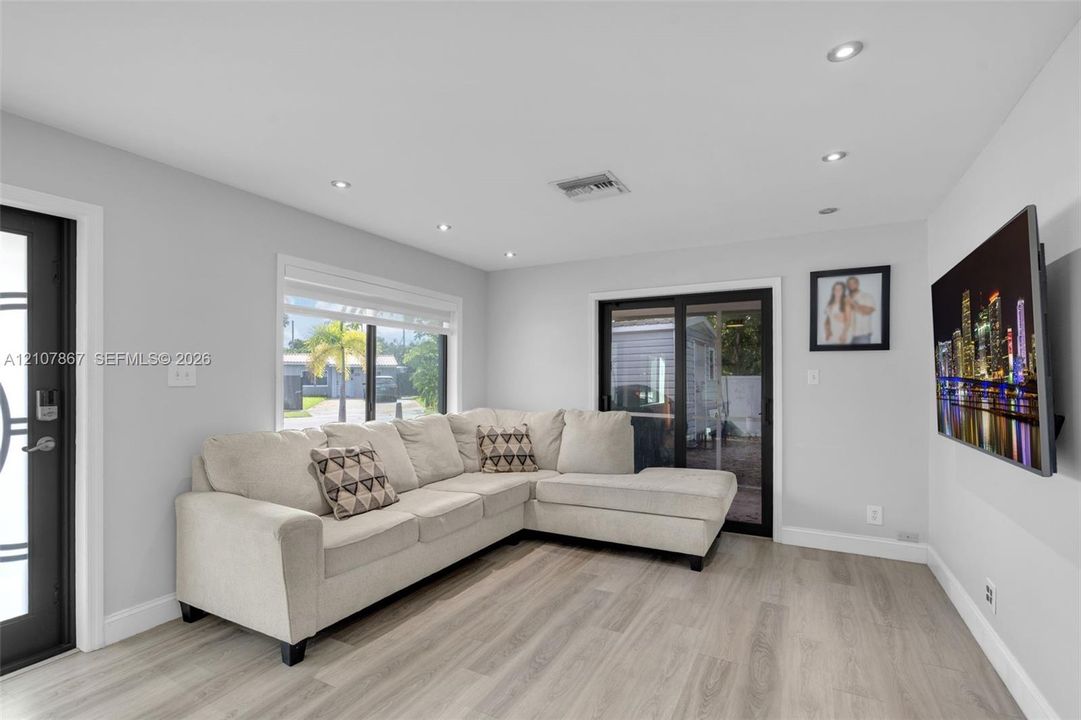 Neutral-toned living space featuring wood-finish flooring, recessed lighting, expansive windows, and glass sliding doors with black frames