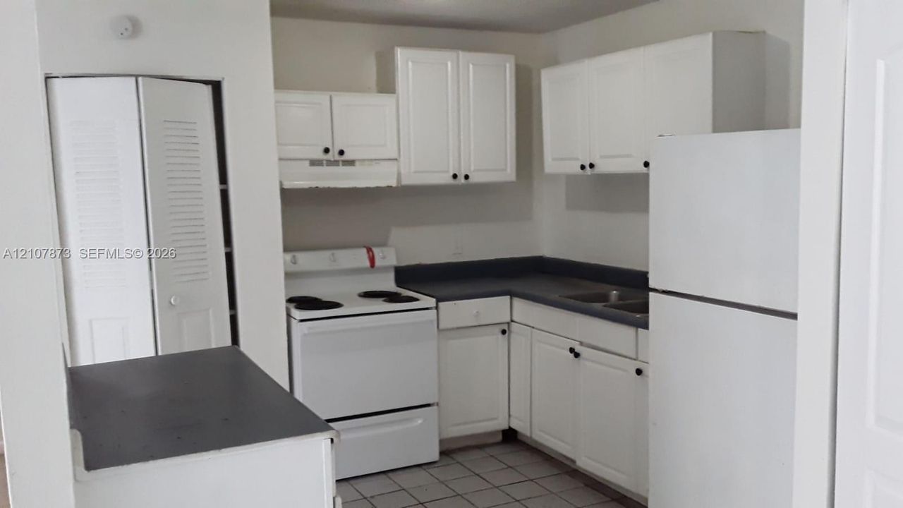 Kitchen featuring white cabinetry, dark countertops, integrated white electric range, and tile flooring