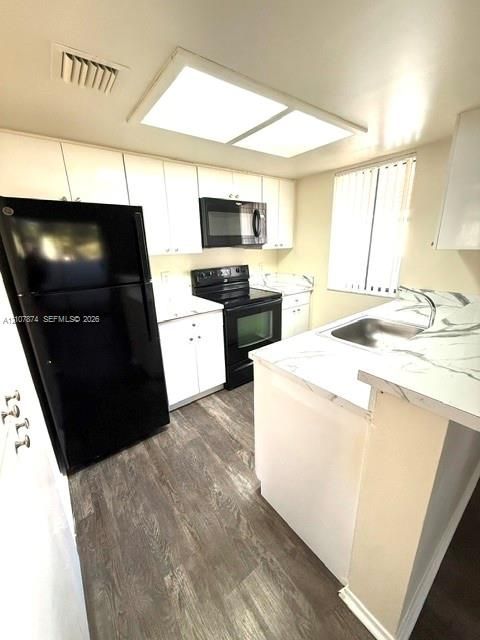 Kitchen featuring white cabinetry, stone-finish countertops, black appliances, a stainless steel sink, and wood-finish flooring