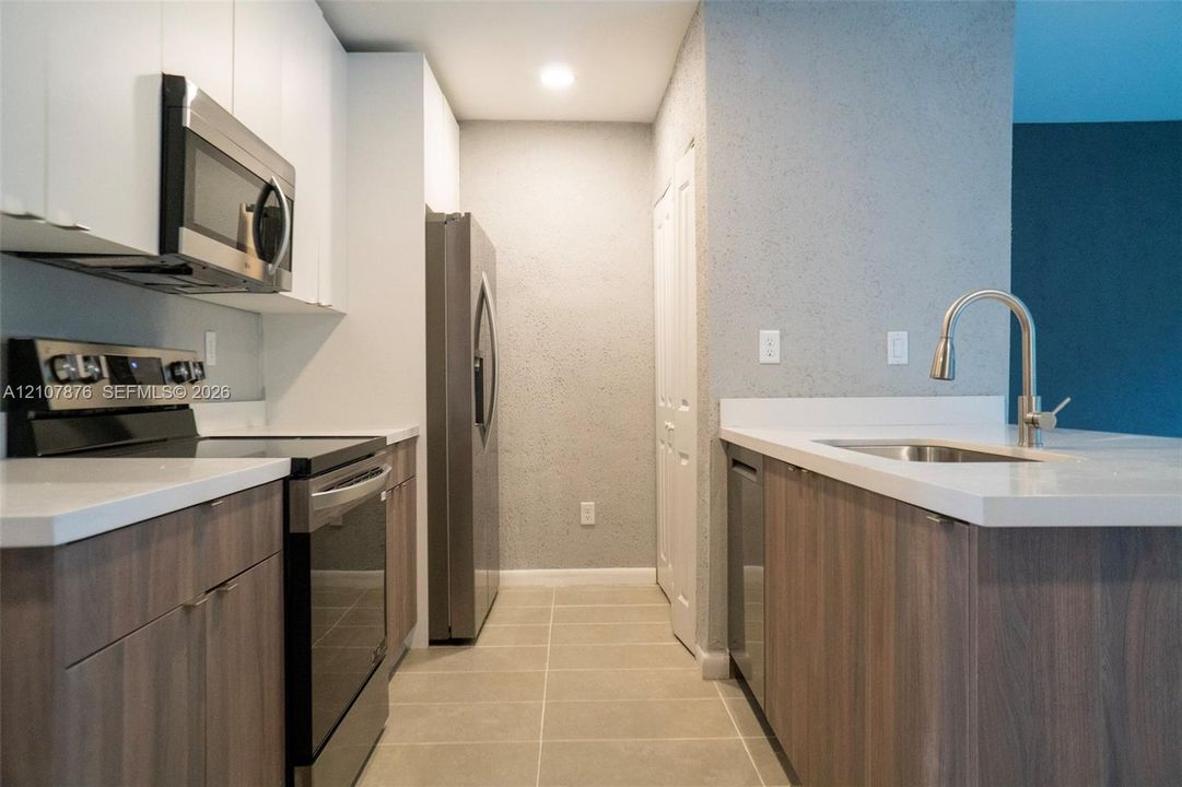 Kitchen featuring two-tone cabinetry with white upper and wood-finish lower units, solid-surface countertops, stainless steel appliances, and tile flooring