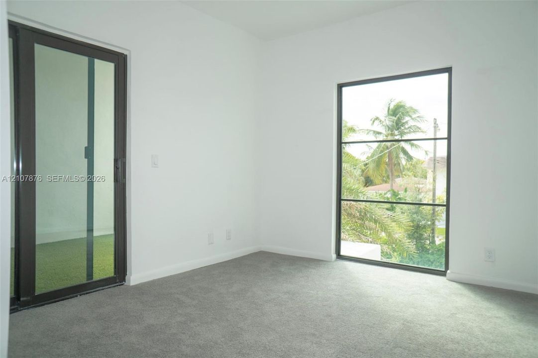 Neutral-toned carpeting, full-height sliding glass door, and large rectangular window with dark-finish frames