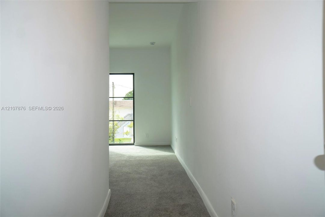 Hallway featuring neutral wall paint, carpeted flooring, and a large window with black mullions