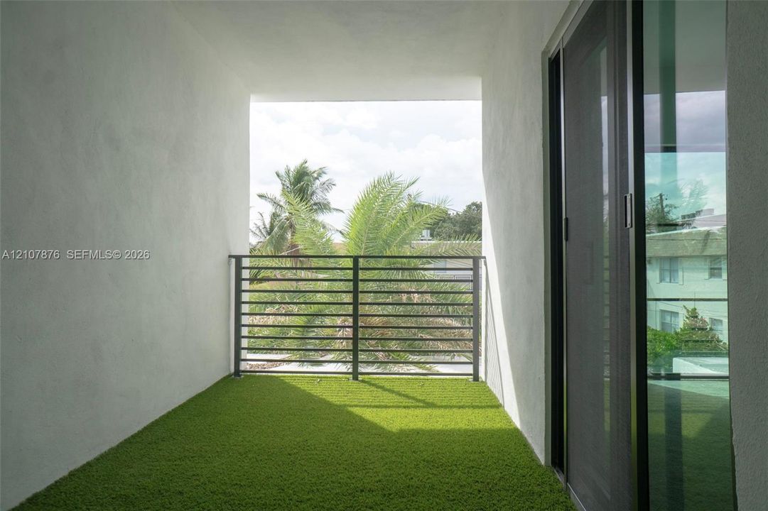 Covered balcony featuring synthetic turf surfacing, horizontal metal railing, and a full-height glass sliding door