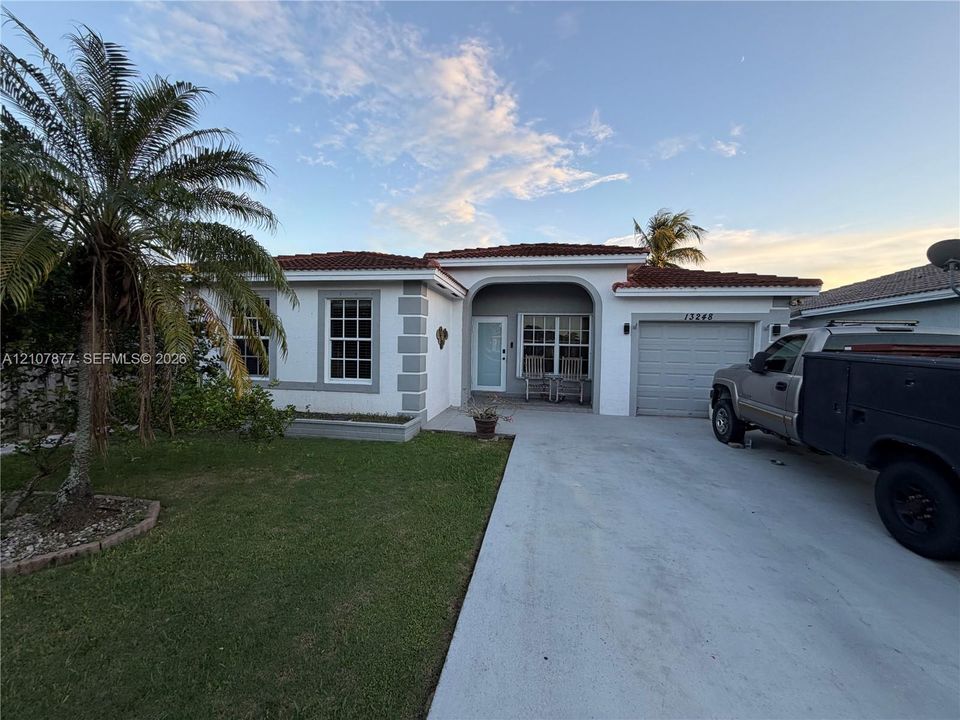 Single-story residence featuring a tile roof, stucco exterior with decorative corner quoins, an arched covered entryway, and a concrete driveway