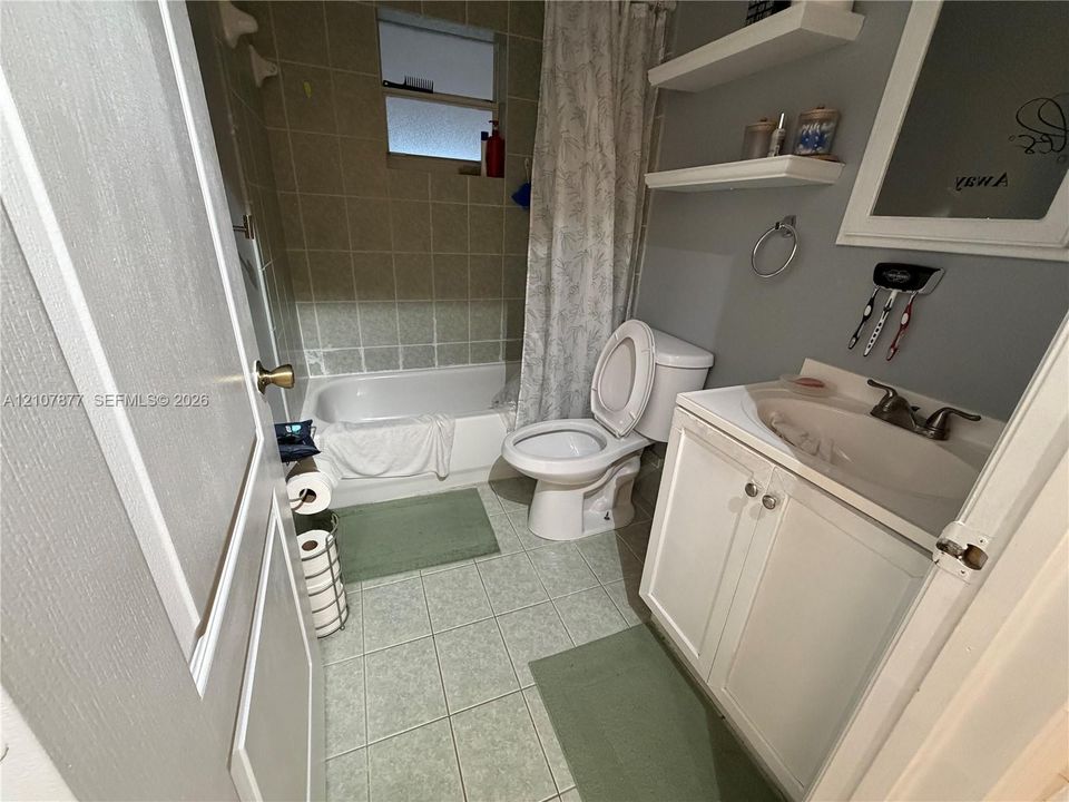 Bathroom featuring a white vanity cabinet with an integrated sink, porcelain tile flooring, a tub-and-shower combination with tile surround, and two built-in wall shelves