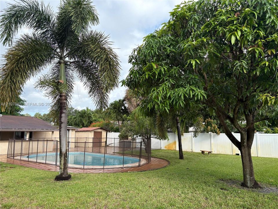Backyard featuring a swimming pool, safety fencing, mature landscaping, and a solid perimeter privacy fence