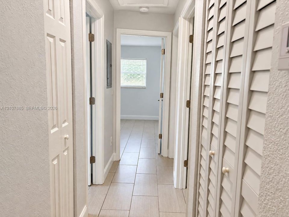 Hallway featuring neutral-toned tile flooring, louvered closet doors, and multiple interior doorways