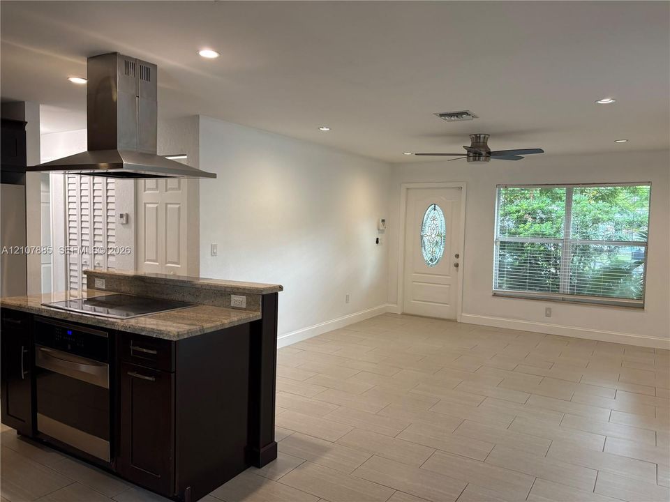 Kitchen peninsula featuring stone-finish countertops, stainless steel chimney-style range hood, dark-toned cabinetry, ceramic tile flooring, and recessed lighting