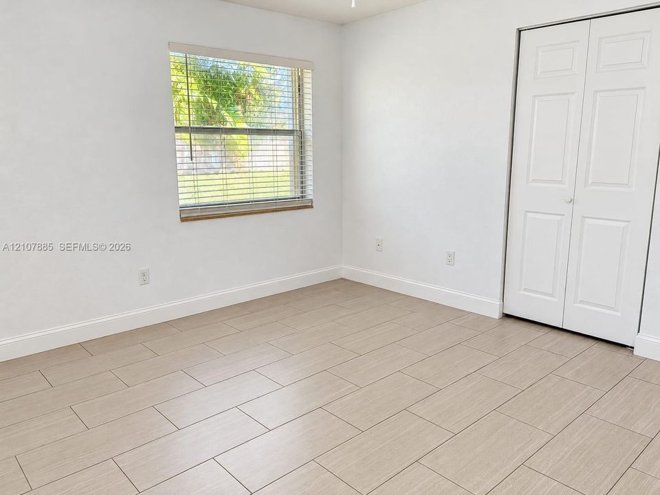 Neutral-toned wood-finish tile flooring, white bi-fold closet doors, and horizontal window blinds