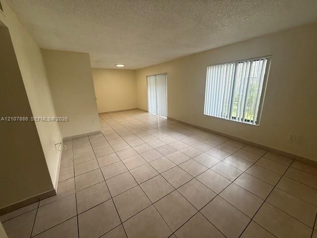 Large living area featuring neutral tile flooring, sliding glass door, oversized window with vertical blinds, and recessed ceiling lighting
