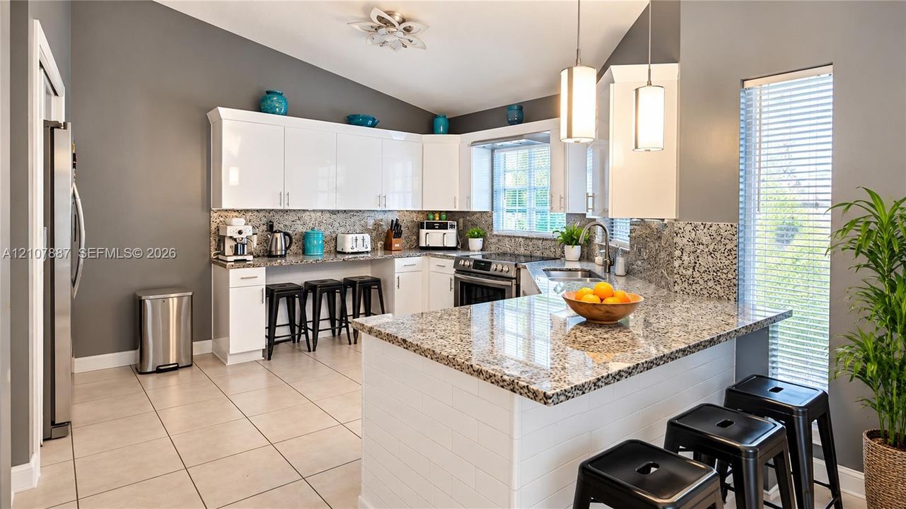 Kitchen featuring white cabinetry, stone-surface countertops, tile flooring, vaulted ceilings, and pendant lighting