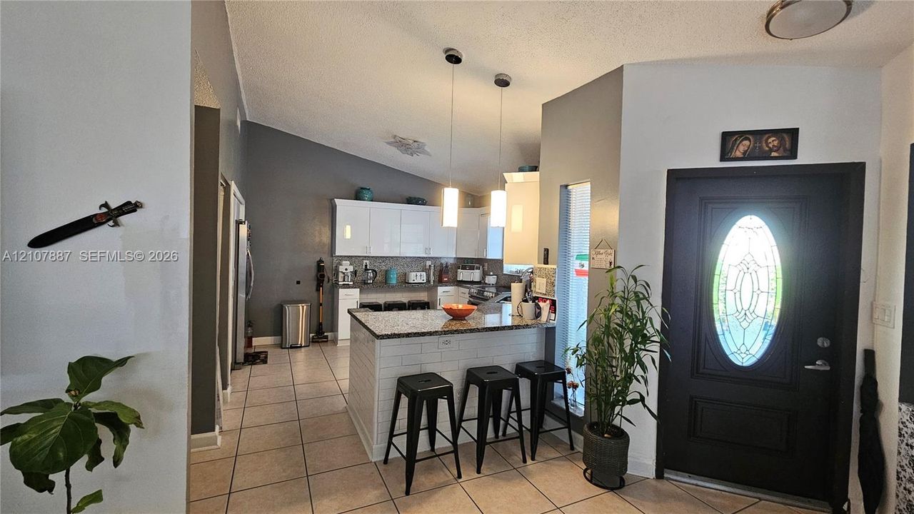 Vaulted ceilings, kitchen island with stone countertop, tile flooring, dual pendant lighting, and entryway door with decorative glass insert