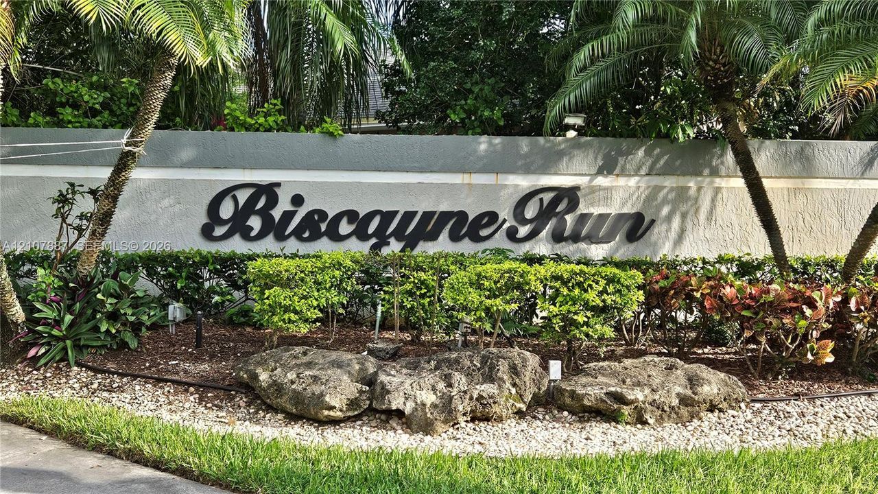 Biscayne Run monument signage featuring a textured masonry wall, dimensional lettering, decorative boulder accents, and professional tropical landscaping