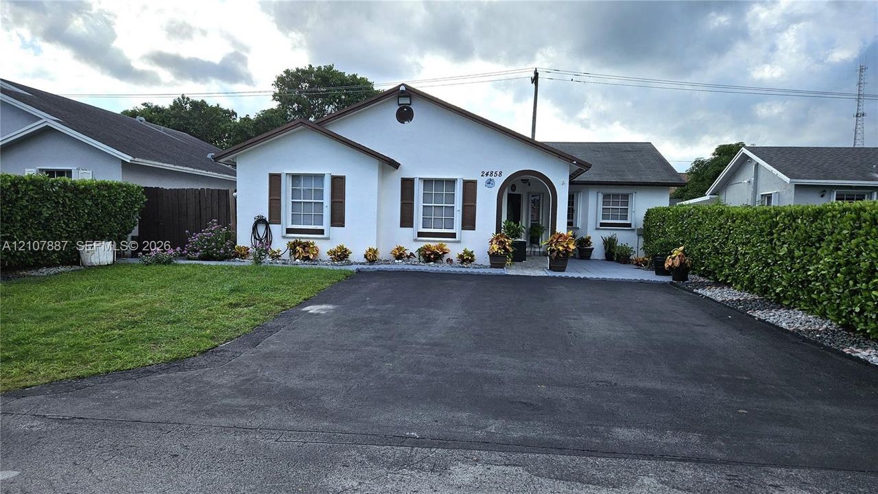Stucco exterior featuring decorative window shutters, an arched entryway, a paved driveway, and established perimeter hedging