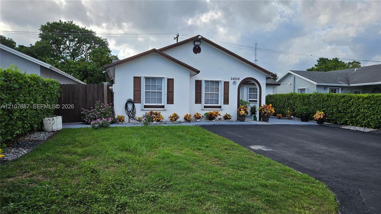 Single-story residence featuring a light-toned exterior, decorative window shutters, an arched entryway, and an asphalt driveway