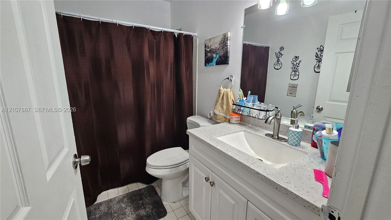 Bathroom featuring a white vanity cabinet, light-colored stone-finish countertop with an integrated basin, high-arc brushed nickel faucet, large wall-mounted mirror, and three-light fixture