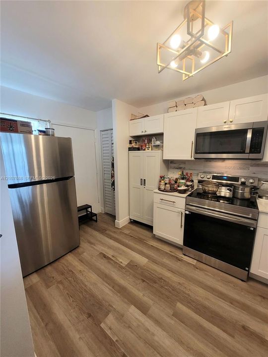 Kitchen featuring white shaker-style cabinetry, stainless steel appliances, wood-finish flooring, and a geometric metal pendant light fixture