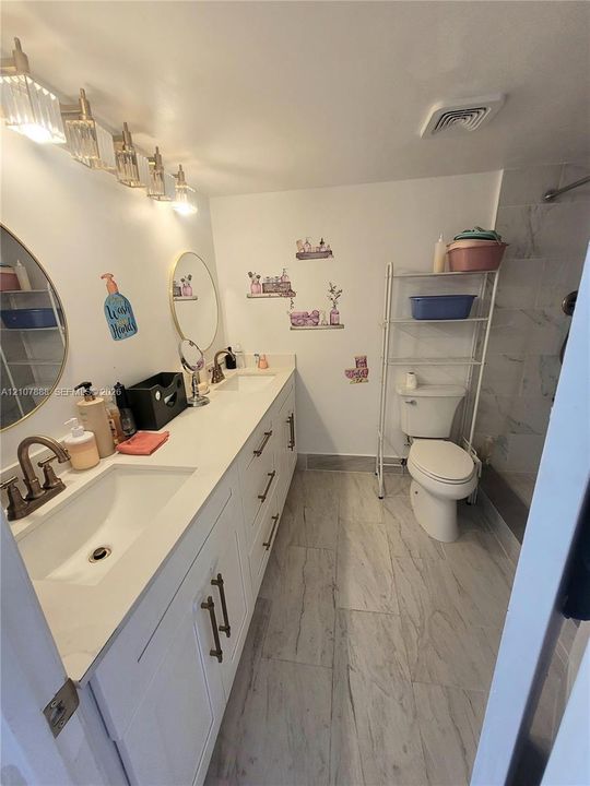 Dual-sink vanity with white cabinetry, light-toned stone-finish countertop, round wall-mounted mirrors, and multi-light fixture