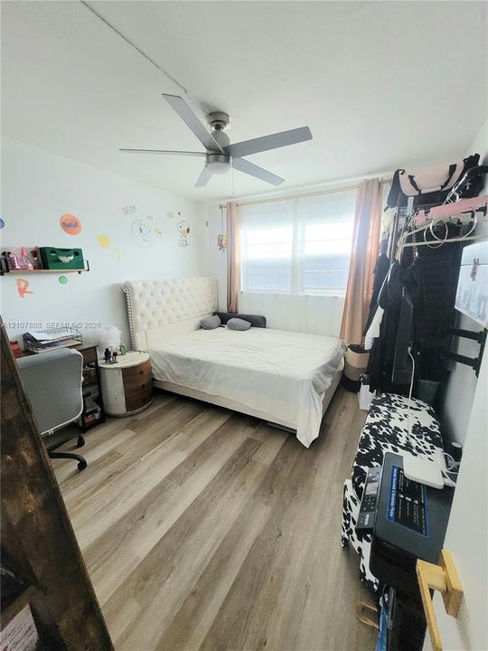 Wood-finish flooring, multi-blade ceiling fan with integrated light fixture, and large window with natural light exposure
