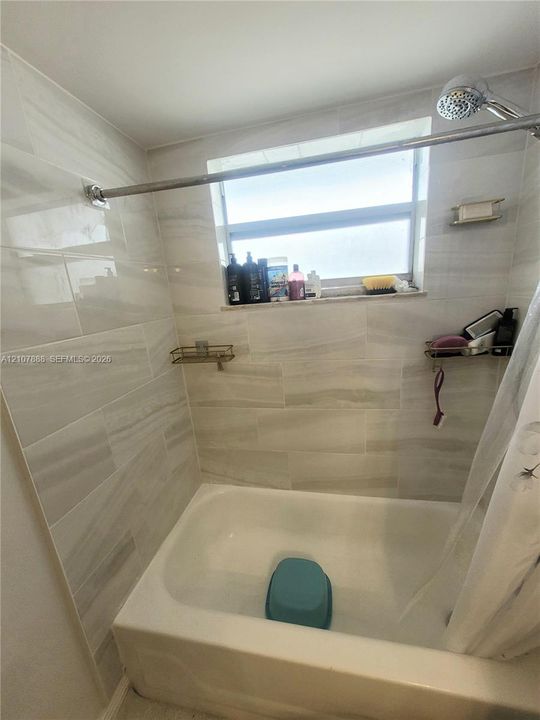 Bathtub and shower combination featuring large-format horizontal tile wall surrounds, a built-in window, and a wall-mounted shower head