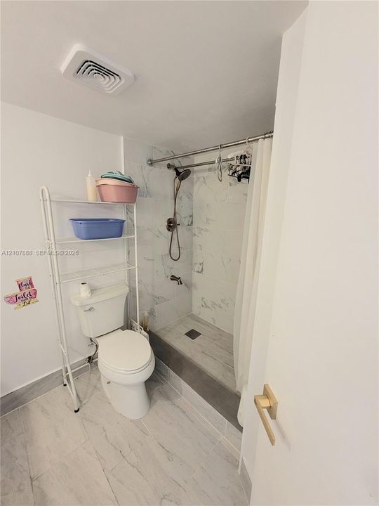 Shower area featuring stone-patterned wall tile, walk-in basin, and metallic shower hardware, complemented by stone-patterned floor tile