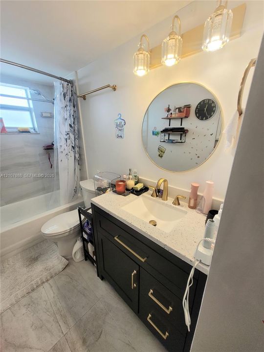 Dark-finish vanity with gold-tone hardware, stone-composite countertop, integrated basin, round gold-rimmed mirror, and three-light wall fixture