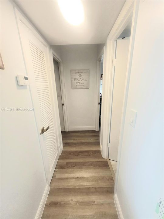 Hallway featuring wood-finish flooring, a louvered closet door, and crisp white interior paint