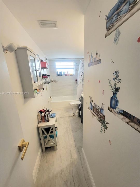 Bathroom featuring light-toned tile flooring, a wall-mounted white storage cabinet, and a bathtub with a tile surround