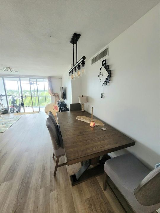 Wood-finish flooring, industrial-style multi-bulb linear pendant lighting, and floor-to-ceiling glass sliding doors opening to a balcony