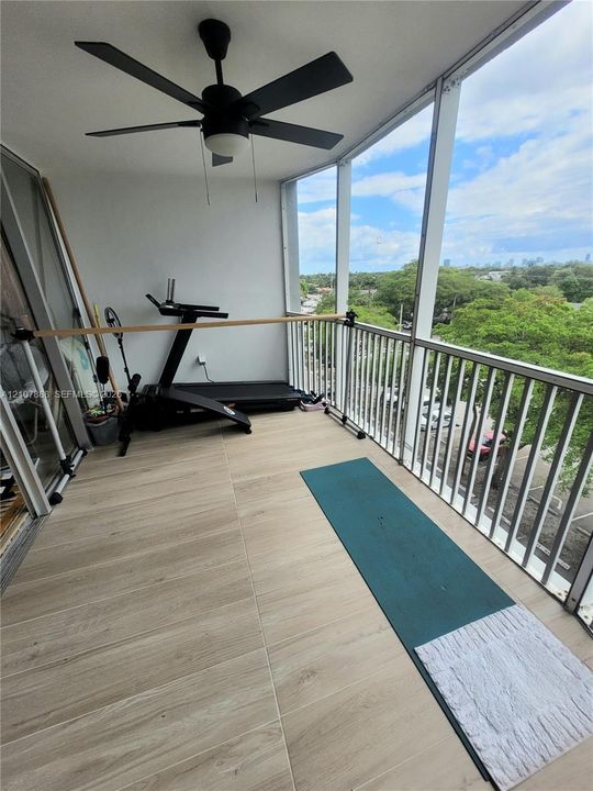 Covered balcony featuring wood-finish tile flooring, white metal railing, and a black ceiling fan