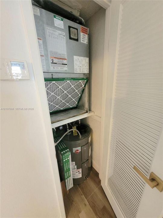 Utility closet containing a dedicated HVAC air handler unit and a water heater, accessed via a louvered door with a metallic finish handle