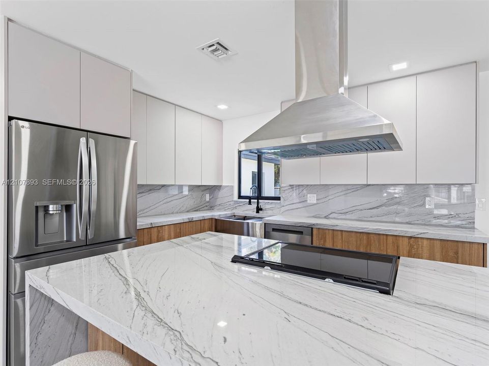 Kitchen featuring floor-to-ceiling flat-panel cabinetry, a central island with a stone countertop, a full-height stone backsplash, stainless steel appliances, and a stainless steel chimney-style range hood