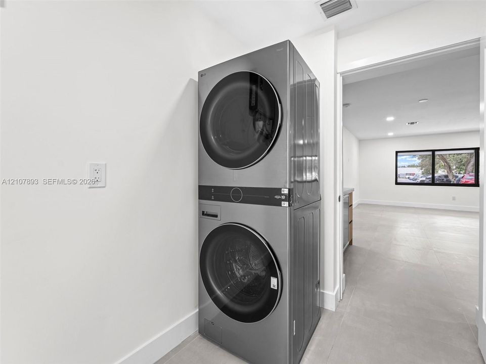 Stainless steel stacked laundry unit featuring front-loading washer and dryer with integrated digital controls and large-format tile flooring
