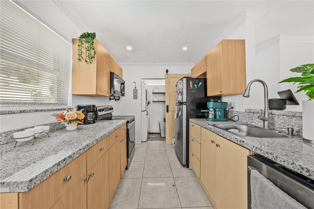 Kitchen featuring light-tone cabinetry, stone-finish countertops, tile flooring, stainless steel appliances, and a sliding barn-style door