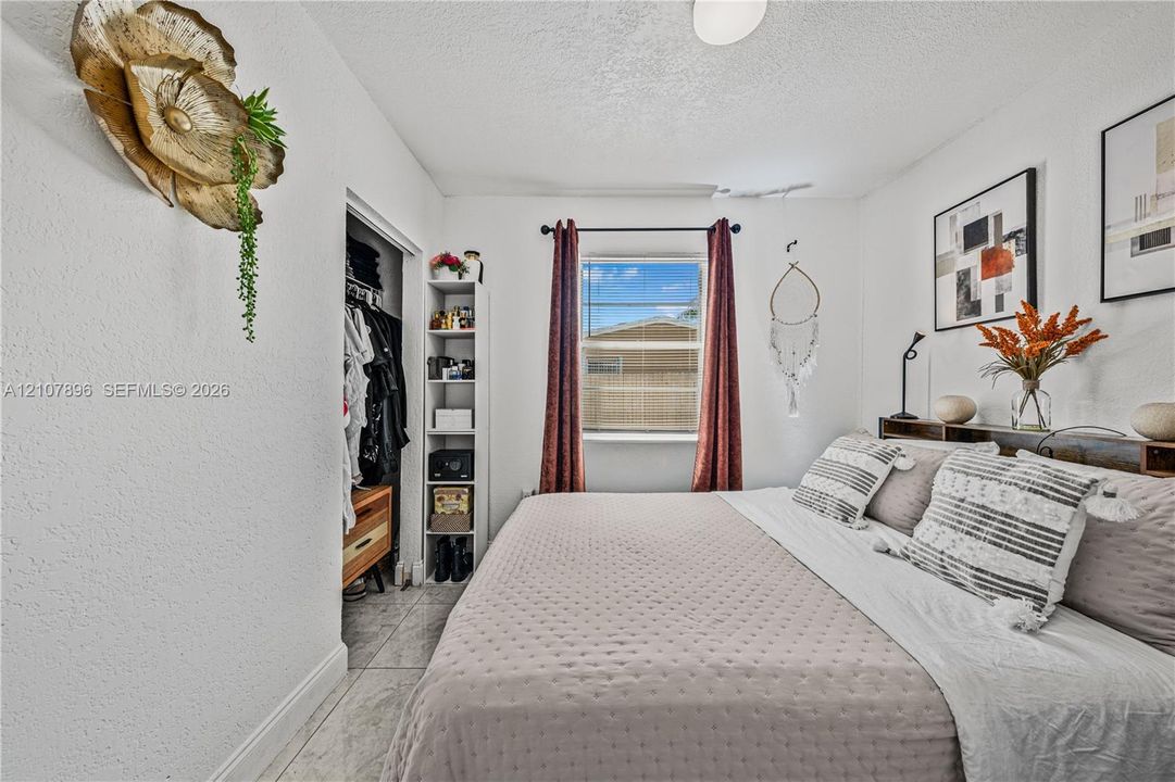 Bedroom featuring neutral wall paint, tiled flooring, and a window with a rod-mounted curtain set