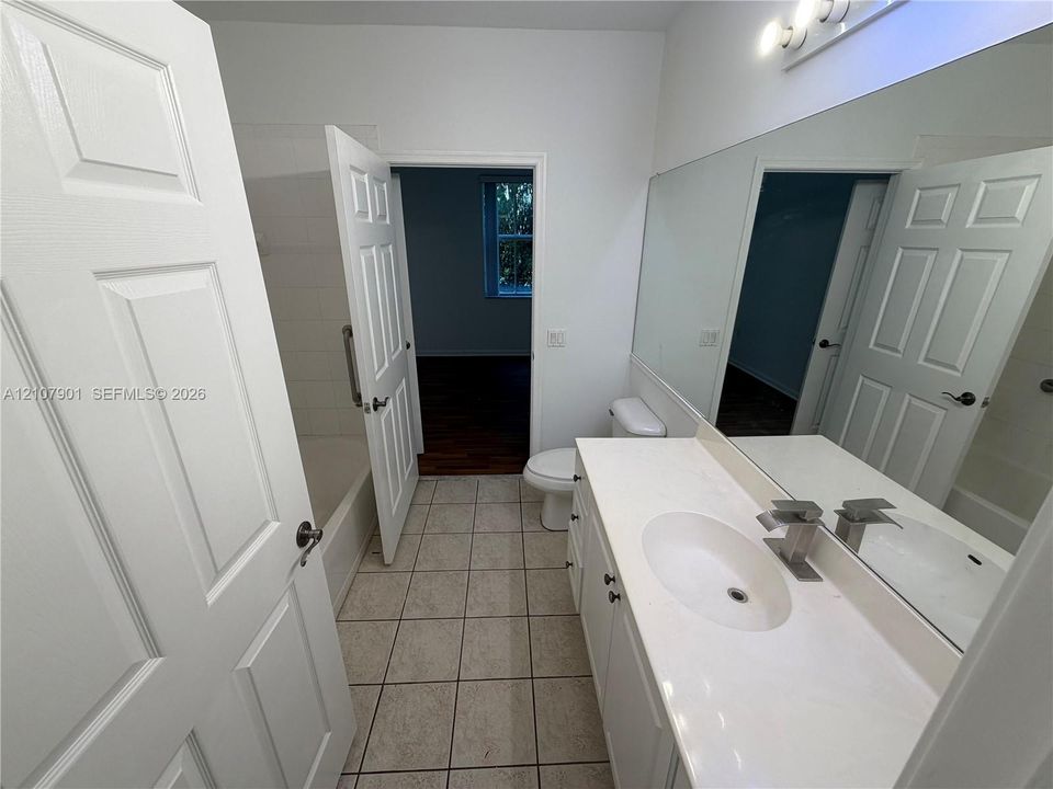 Bathroom featuring a white vanity with a solid-surface countertop, an integrated oval sink, a large wall-mounted mirror, and tile flooring