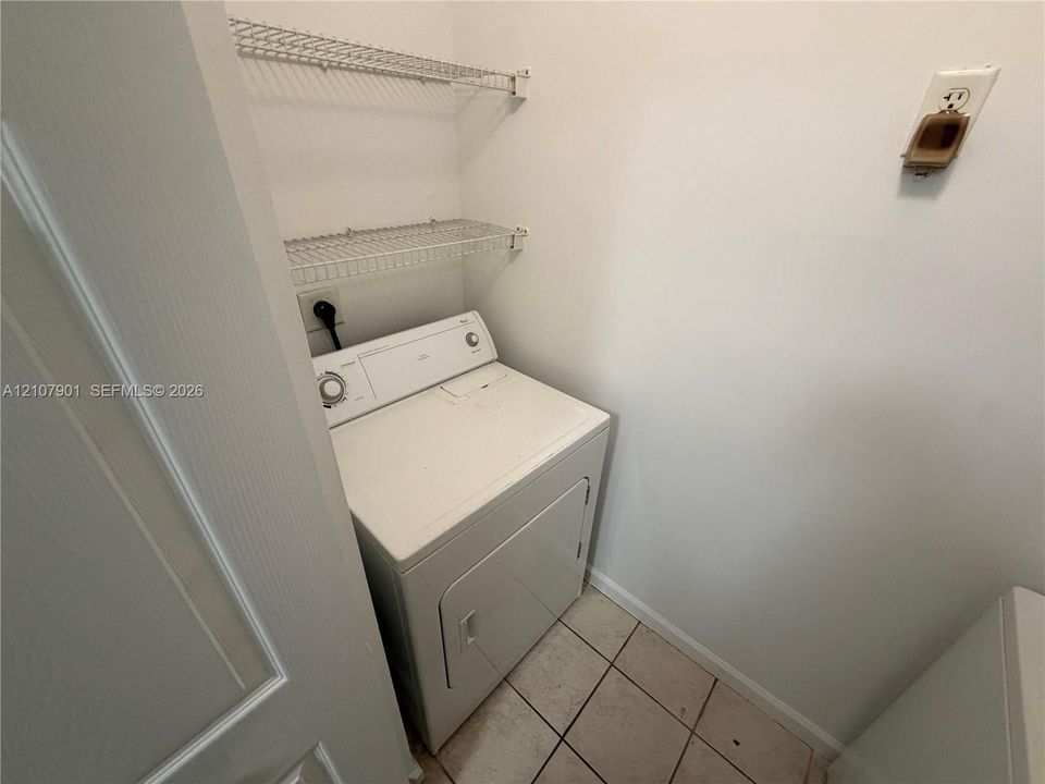 Laundry area featuring tile flooring, white-finish walls, and dual-tier wire shelving